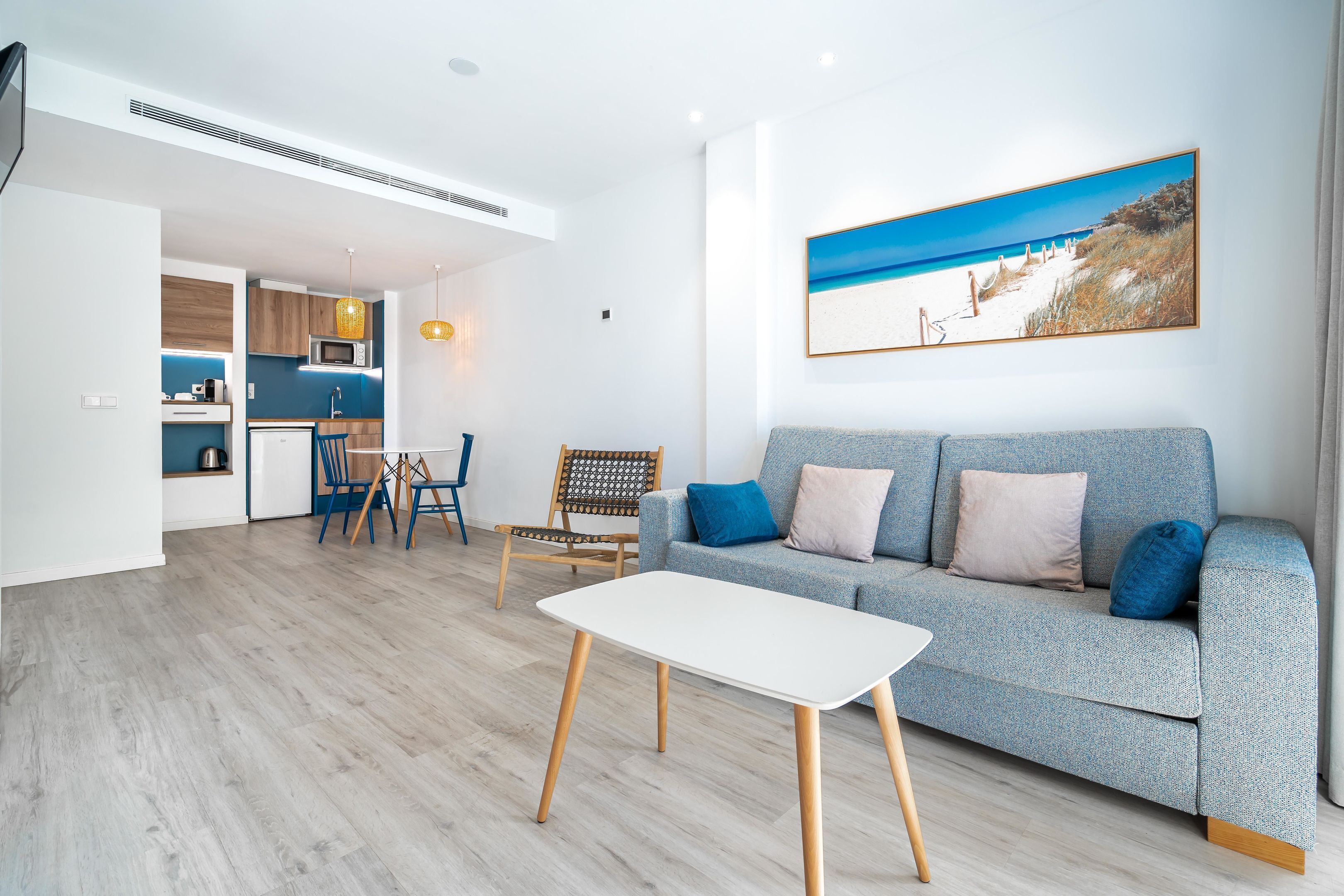 A modern living room with a grey sofa, a white coffee table, and a dining area with a wooden table and chairs.