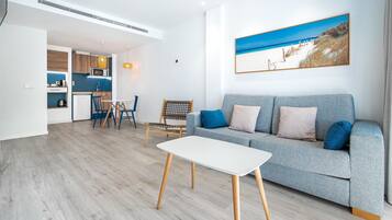A modern living room with a grey sofa, a white coffee table, and a dining area with a wooden table and chairs.