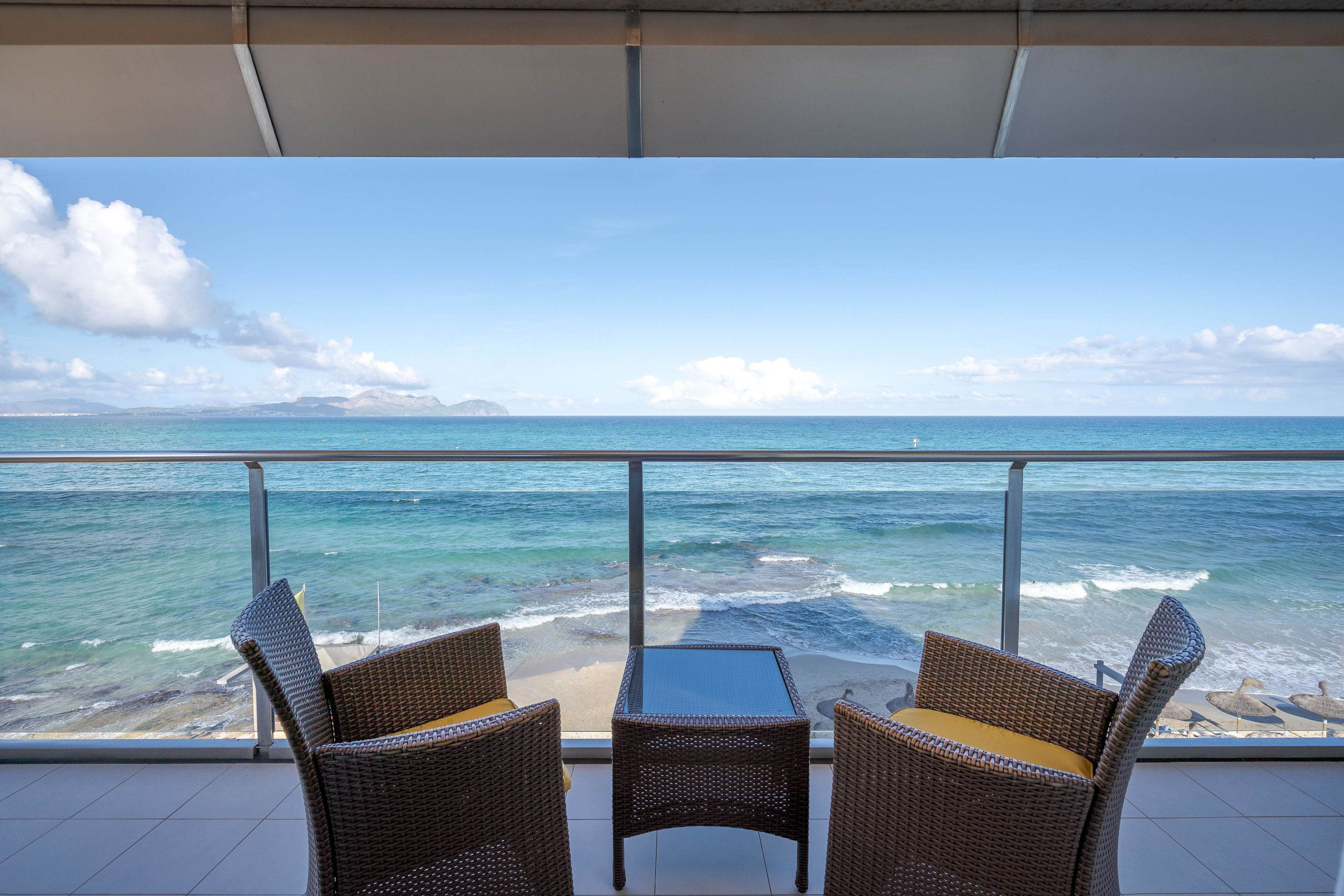 Un balcón con muebles de mimbre con vista a una playa y al océano.