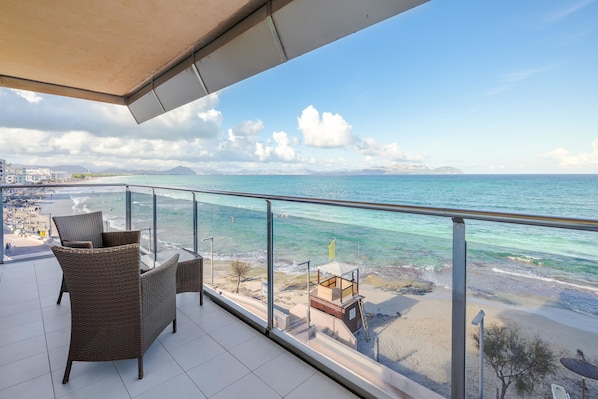 Ein Balkon mit Korbmöbeln, der Blick auf Strand und Meer freigibt.