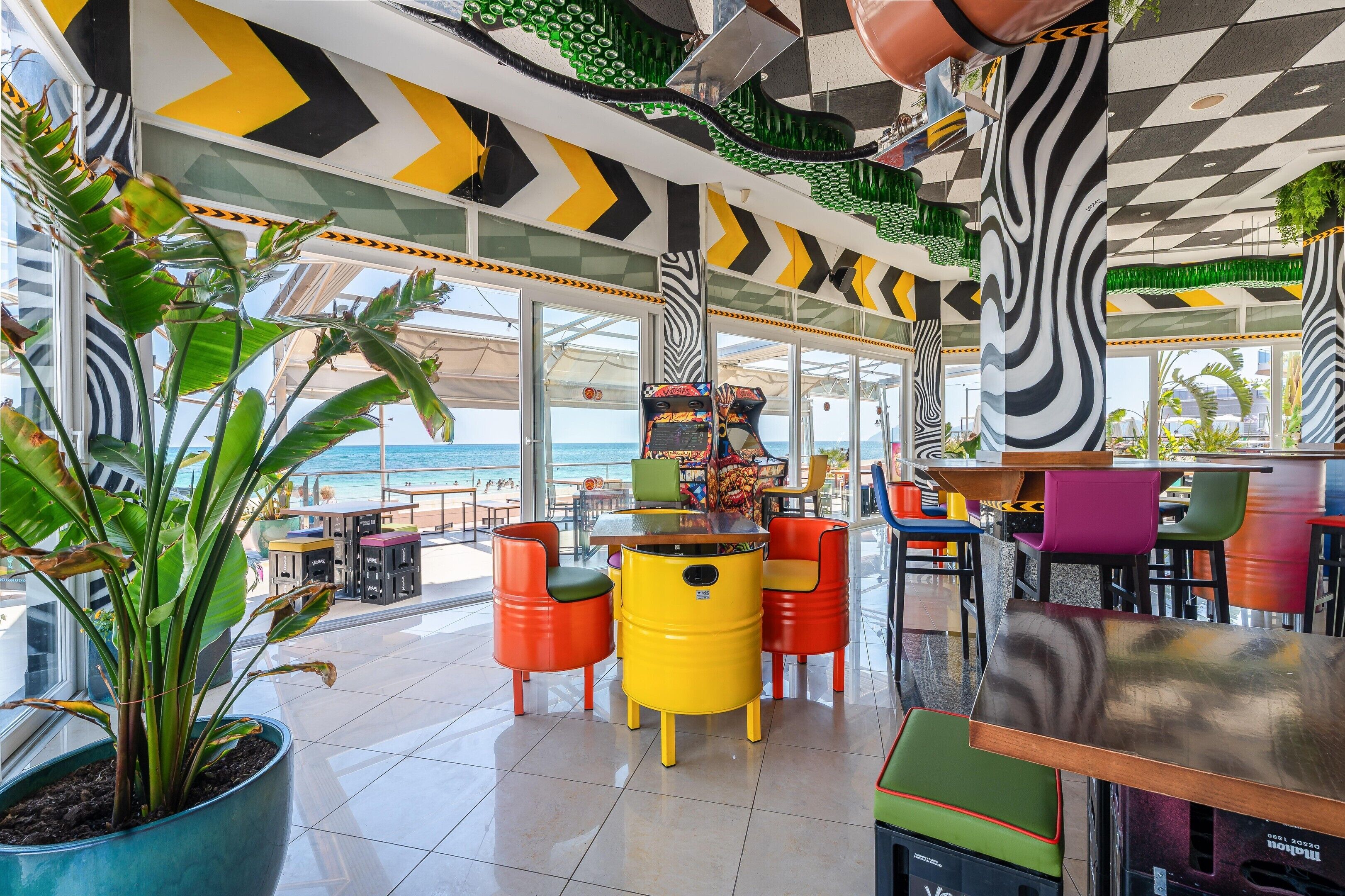 Un restaurant animé, avec des tabourets aux couleurs vives et une vue sur la mer.