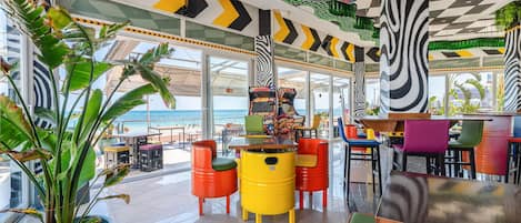 Un restaurant animé, avec des tabourets aux couleurs vives et une vue sur la mer.