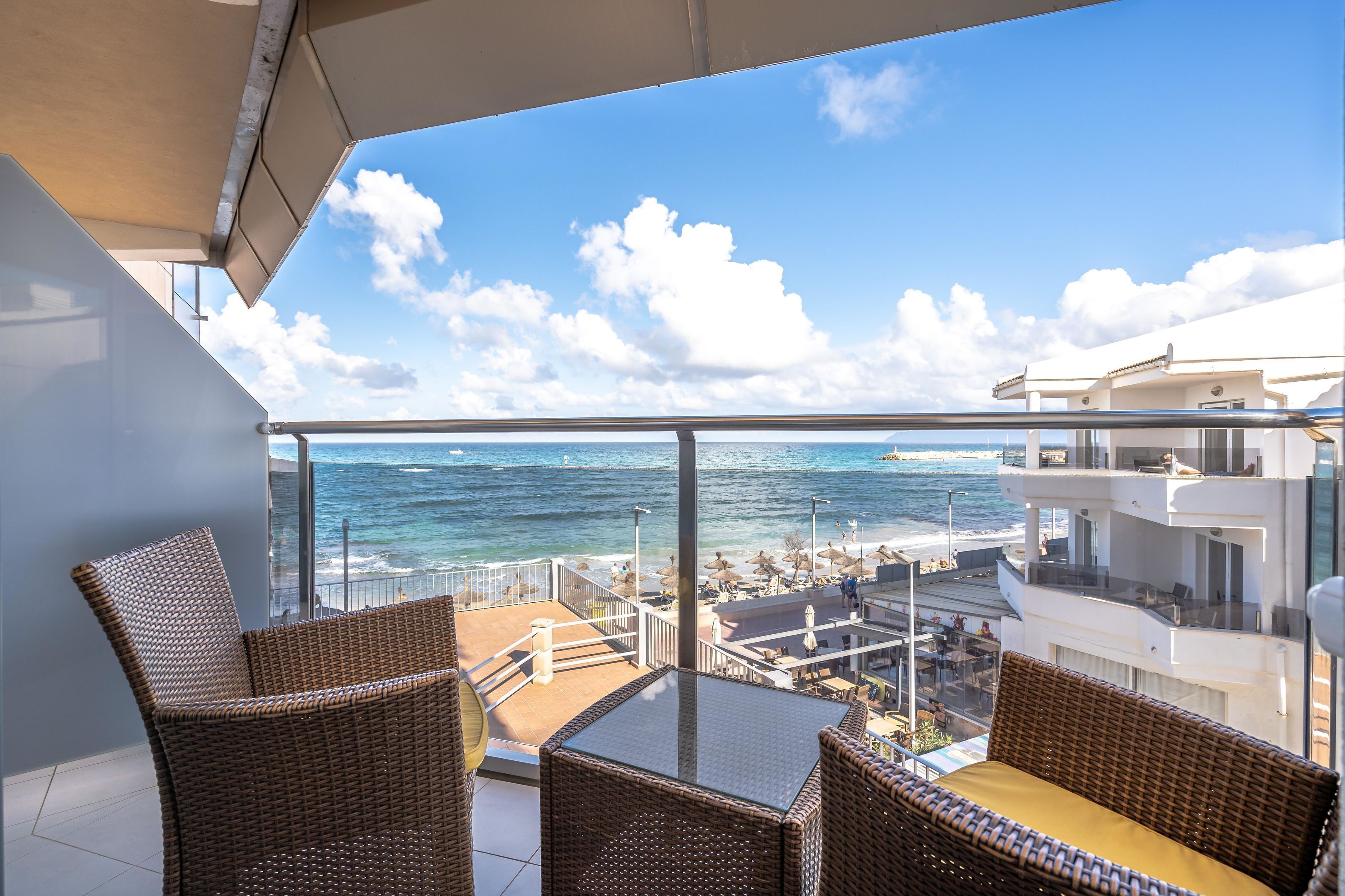 A balcony with wicker furniture overlooking a beach and ocean.