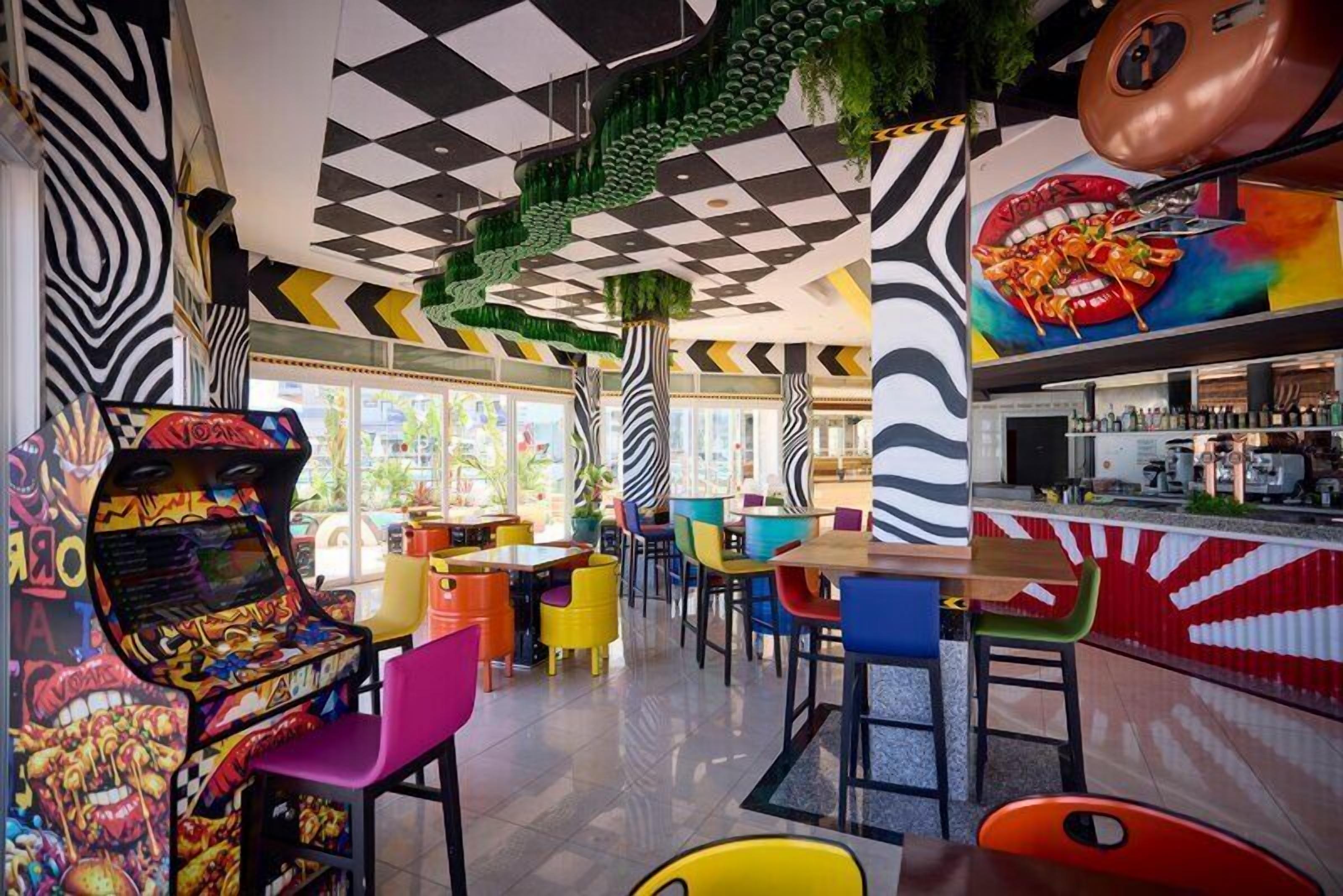 A vibrant arcade with colorful gaming machines, a bar area with a red and white striped counter, and a variety of seating options.