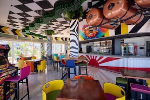 Ein Restaurant mit bunten Stühlen, einer Theke mit rot-weißer Gestaltung und einer Decke mit geometrischem Muster.