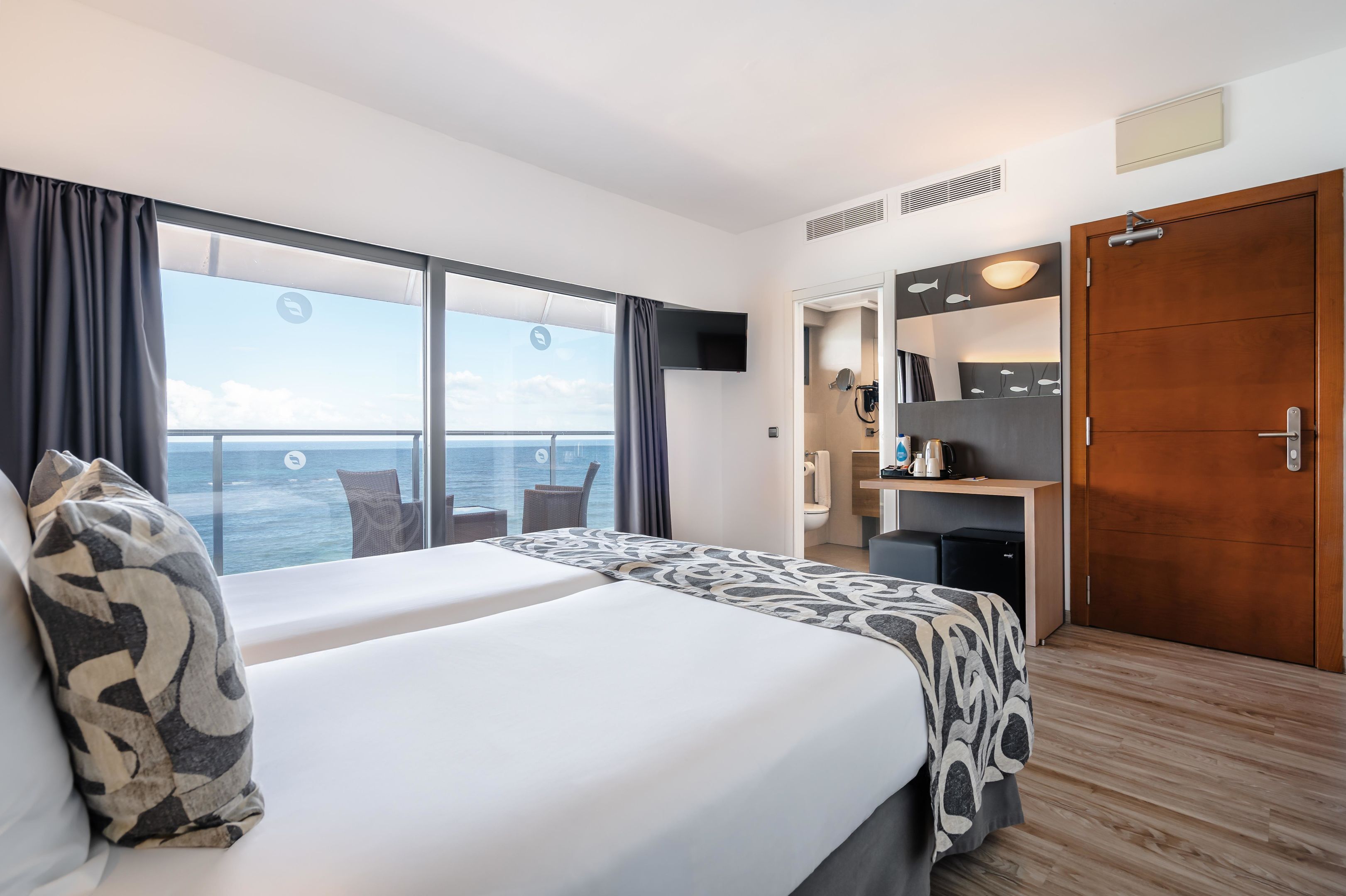 Une chambre d’hôtel avec un grand lit, un bureau, une armoire et une vue sur la mer.