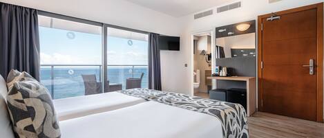 A hotel room with a large bed, a desk, a wardrobe, and a view of the sea.