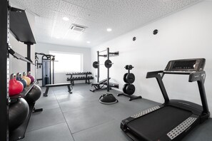 A gym with a treadmill, weight bench, kettlebells, dumbbells, and a squat rack. - THB Gran Bahia Hotel and Apartments (Santa Margalida)