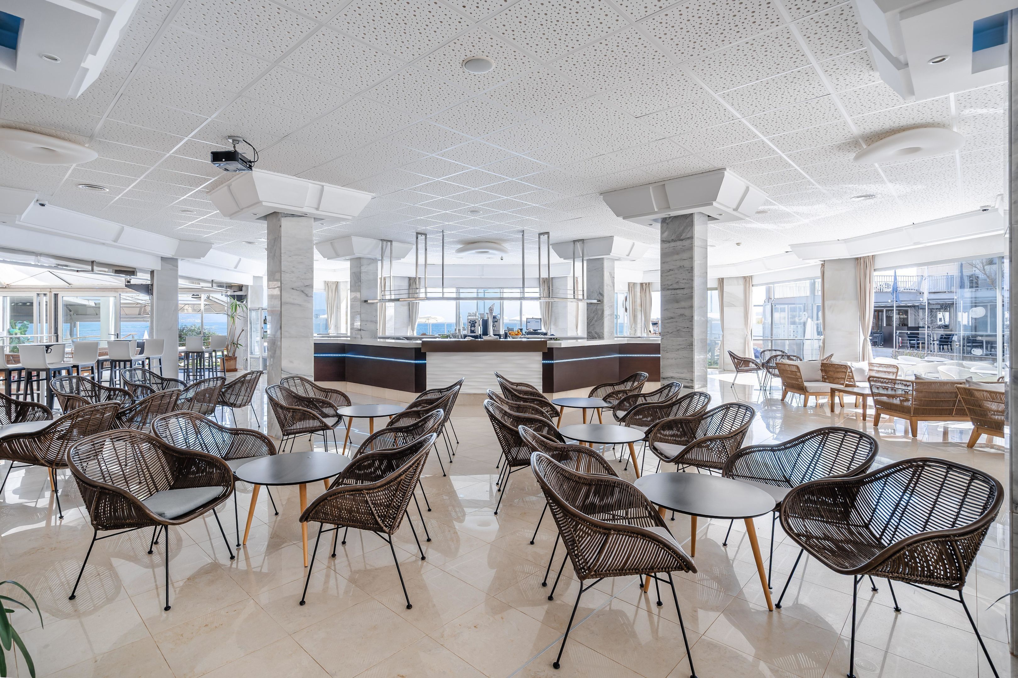 A spacious indoor area with wicker chairs and tables, large windows, and a central counter.