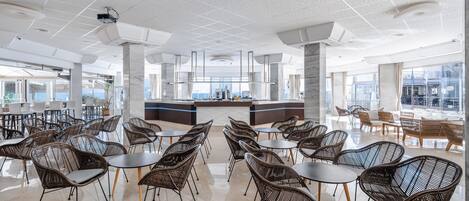 A spacious indoor area with wicker chairs and tables, large windows, and a central counter.