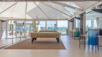 A pool table in a spacious room with large windows overlooking a pool area.