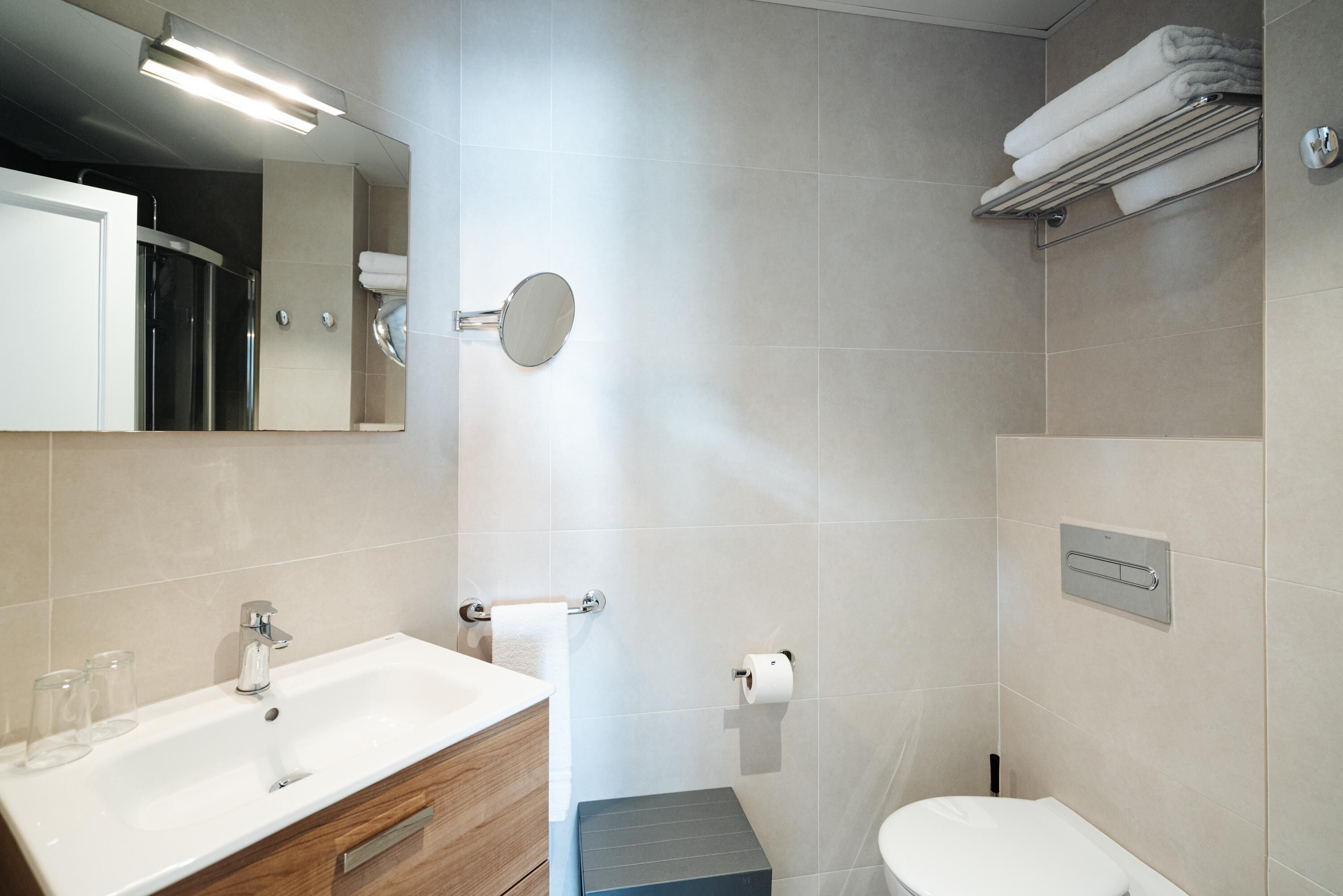 Un baño moderno con lavamanos, espejo, inodoro y toallero.