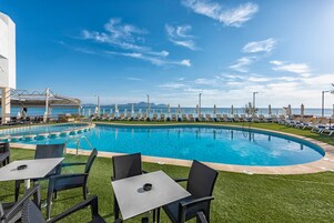 Área da piscina com espreguiçadeiras e mesas, céu claro e vista para o mar.