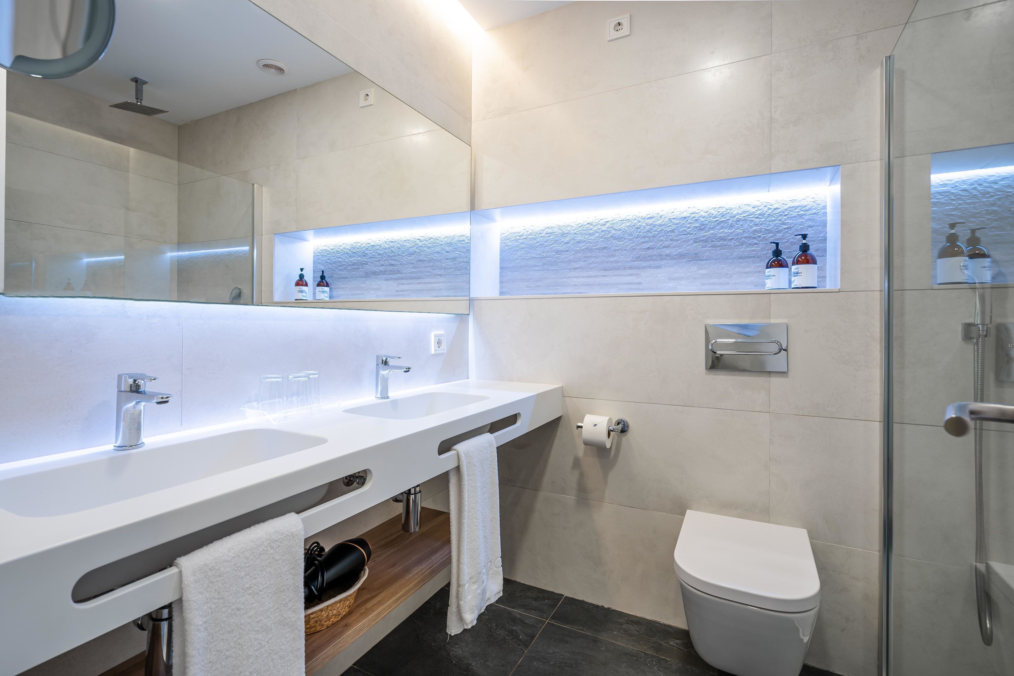 Uma casa de banho moderna com duas pias, sanita e cabine de duche em vidro.