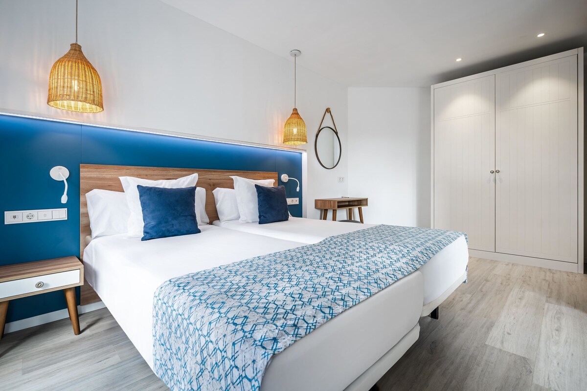 Une chambre moderne avec un grand lit, des tables de chevet, une armoire et des luminaires suspendus.