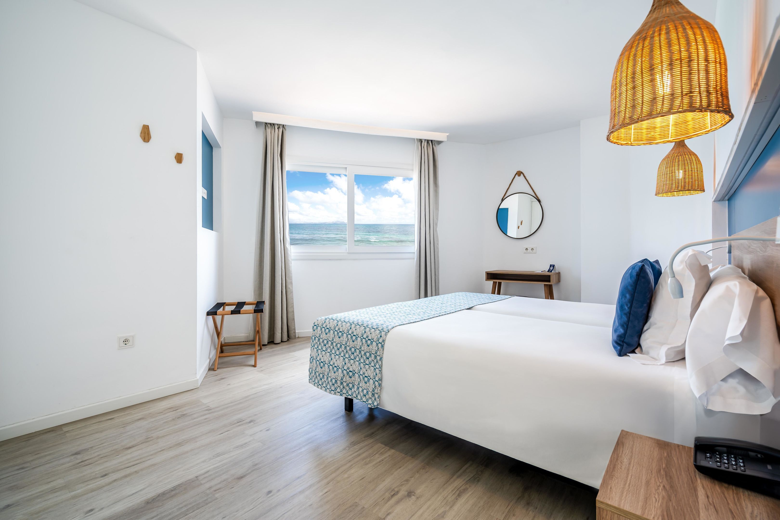 Een hotelkamer met een bed, een tafeltje, een stoel, een raam met uitzicht op zee en een hanglamp.