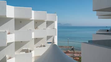 A modern building with white balconies overlooking a clear blue sea.