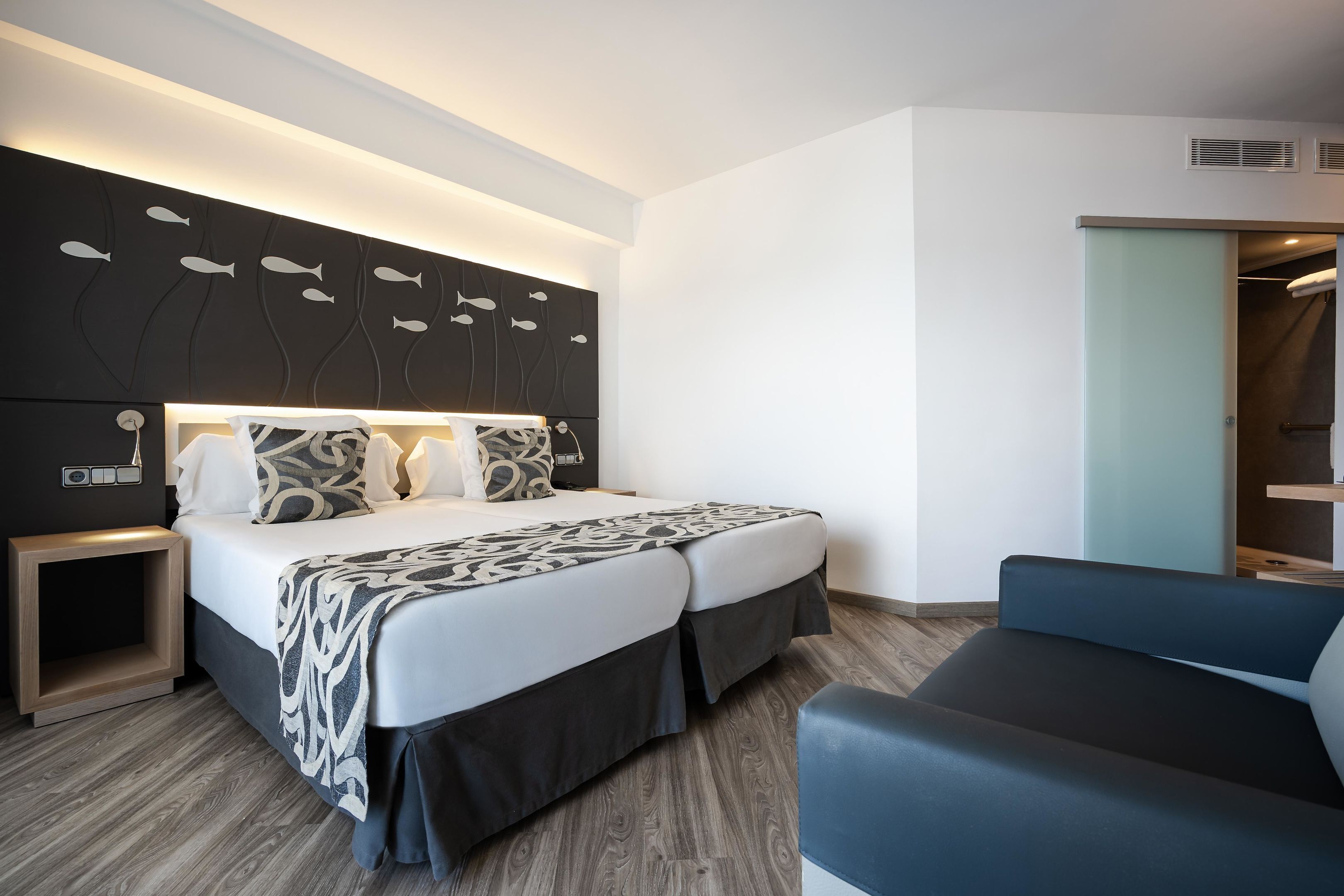 Una habitación de hotel moderna con una cama grande, mesitas de noche, una zona de estar y un armario.