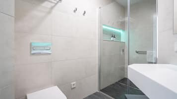 Un baño moderno con cabina de ducha de vidrio, un lavabo blanco y un inodoro.