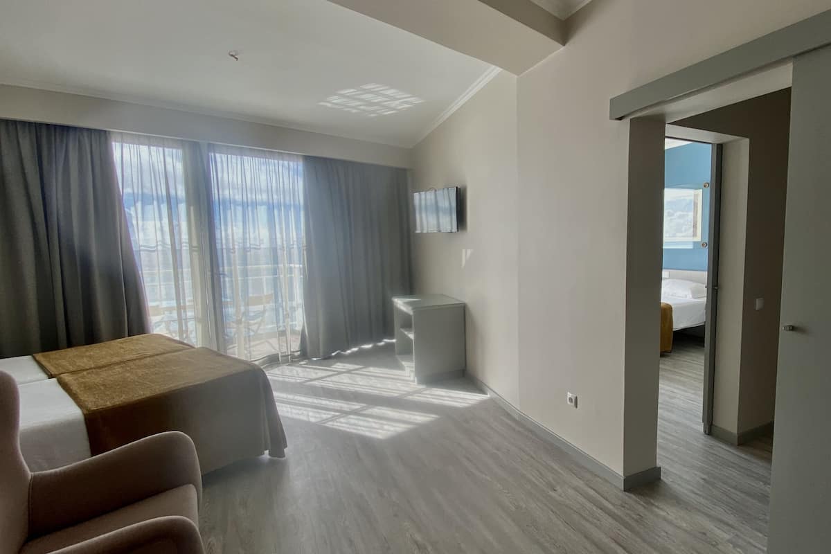 A hotel room with a bed, a desk, a chair, a TV, and a view of the city through large windows.