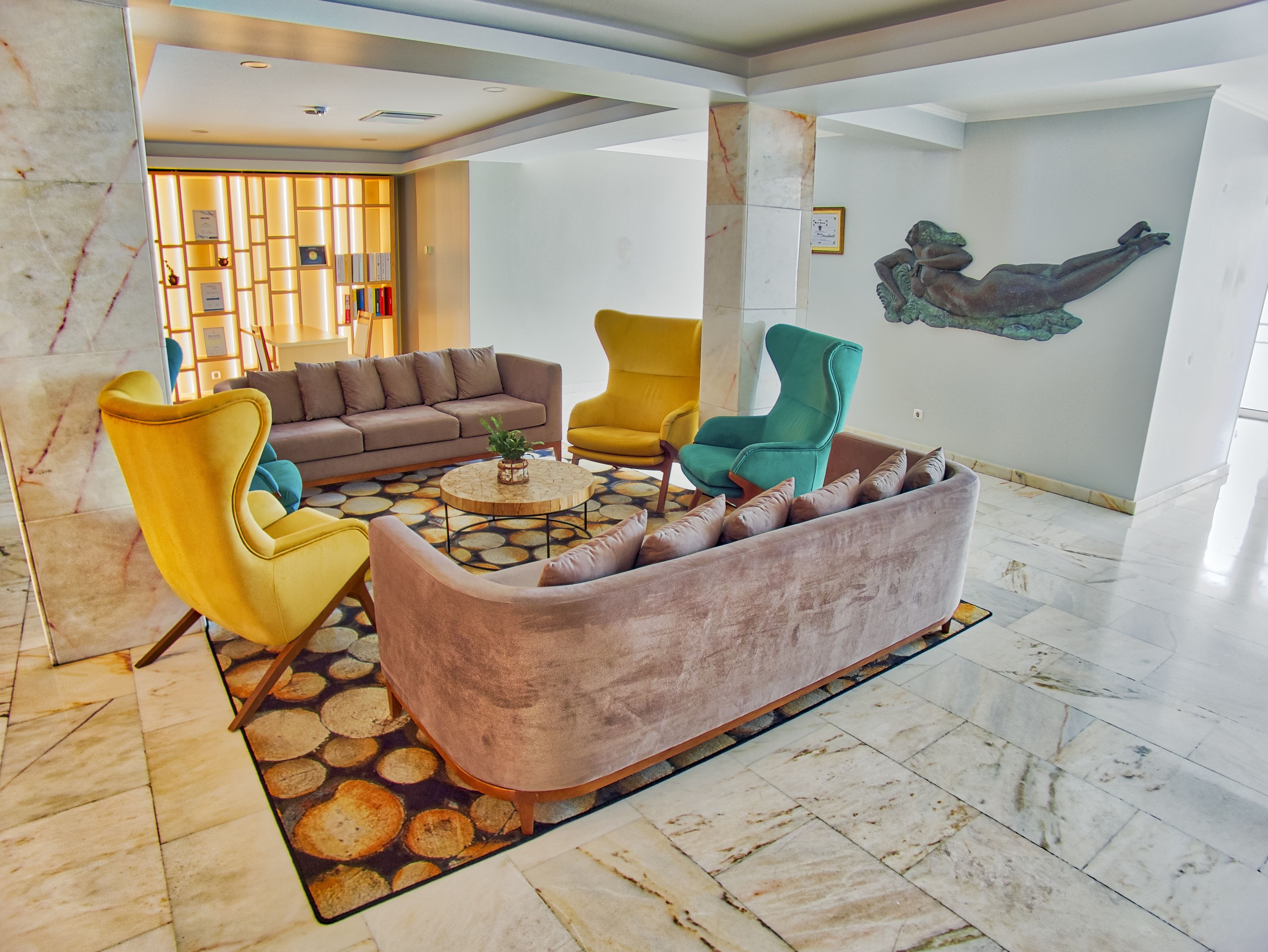 Um lobby moderno com piso de mármore, área de estar central com sofá e poltronas, mesa de centro e uma escultura na parede.