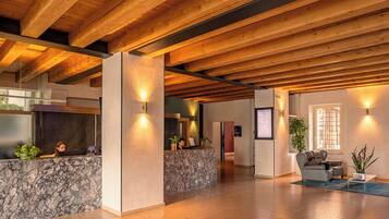 A spacious lobby with a marble reception desk, wooden ceiling beams, and a seating area with a sofa and armchairs.