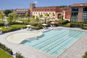 A swimming pool with lounge chairs and umbrellas, surrounded by well-maintained gardens and a building with a red facade.
