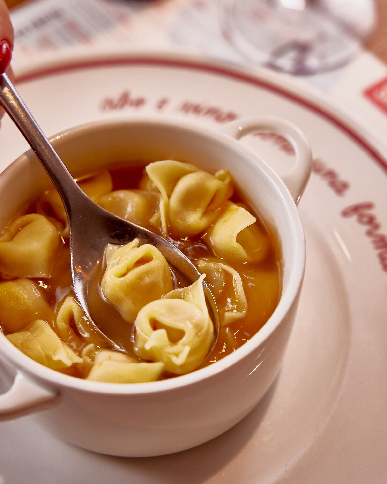 A bowl of soup with dumplings and a spoon.