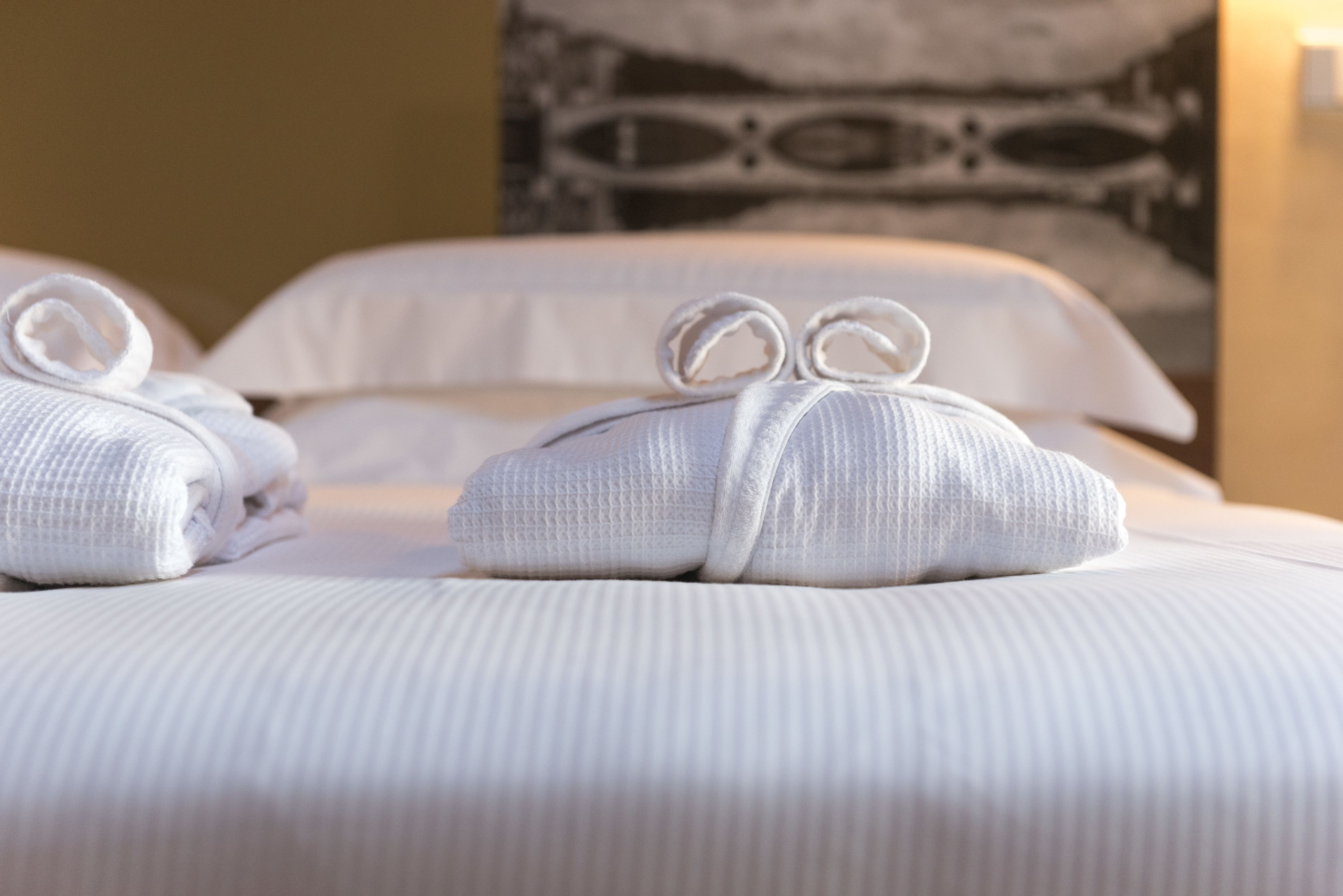 A neatly made bed with two towels folded and tied with a bow, a pillow, and a patterned wall in the background.