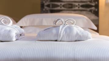Ein ordentlich gemachtes Bett mit zwei mit einer Schleife gebundenen Handtüchern, einem Kopfkissen und einer gemusterten Wand im Hintergrund.