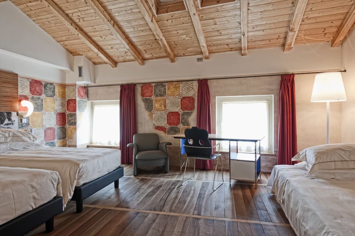 A hotel room with two beds, a desk, and a chair. The room has wooden flooring and a sloped ceiling.
