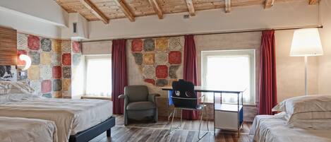 Habitación de hotel con dos camas, un escritorio y una silla. La habitación tiene suelo de madera y techo inclinado.