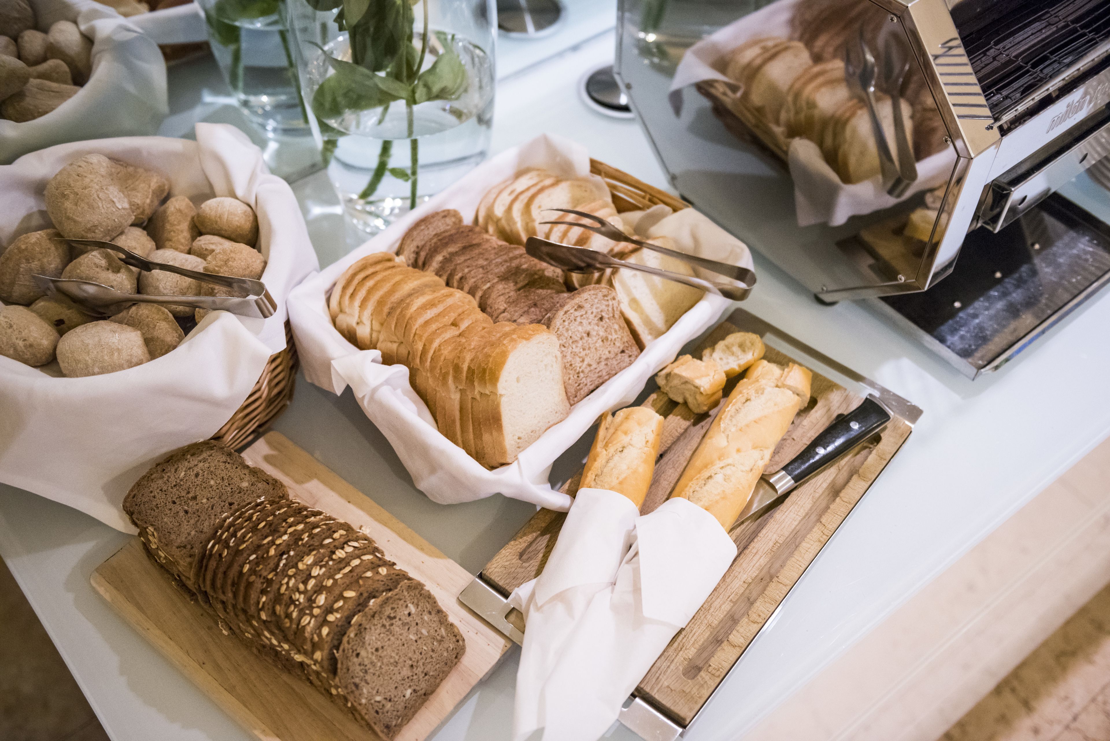 Variedad de panes y pasteles sobre una mesa, incluyendo barras de pan francesas, pan integral y otras preparaciones horneadas.