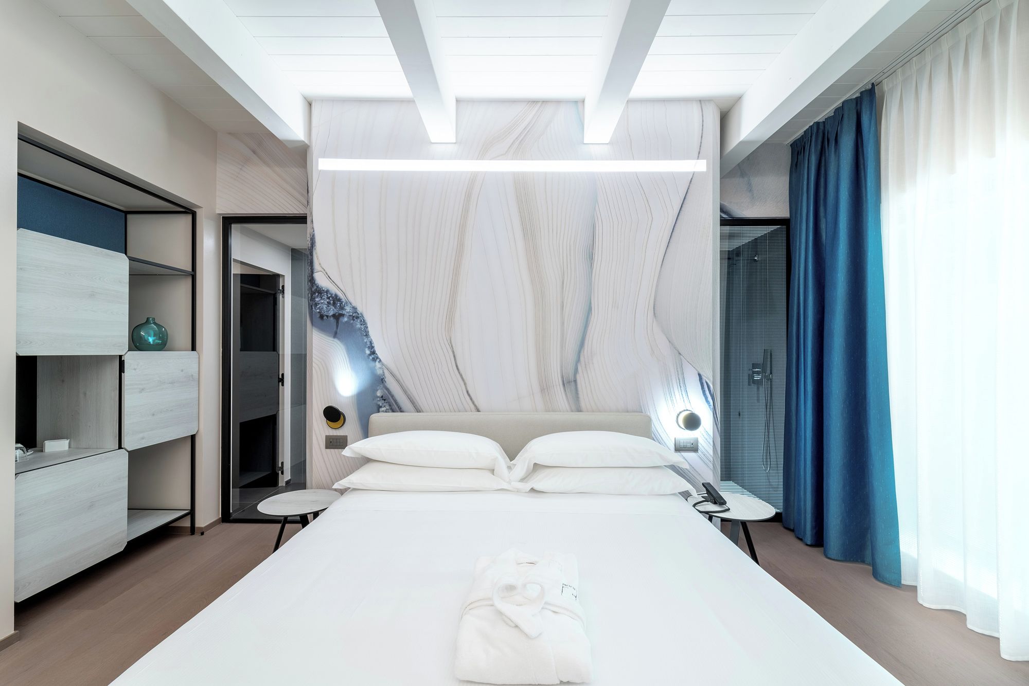 Una habitación de hotel moderna con una cama grande, mesitas de noche, un armario y un baño con ducha.