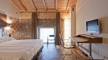 A bedroom with a bed, a desk, a chair, a television, and a stone wall.