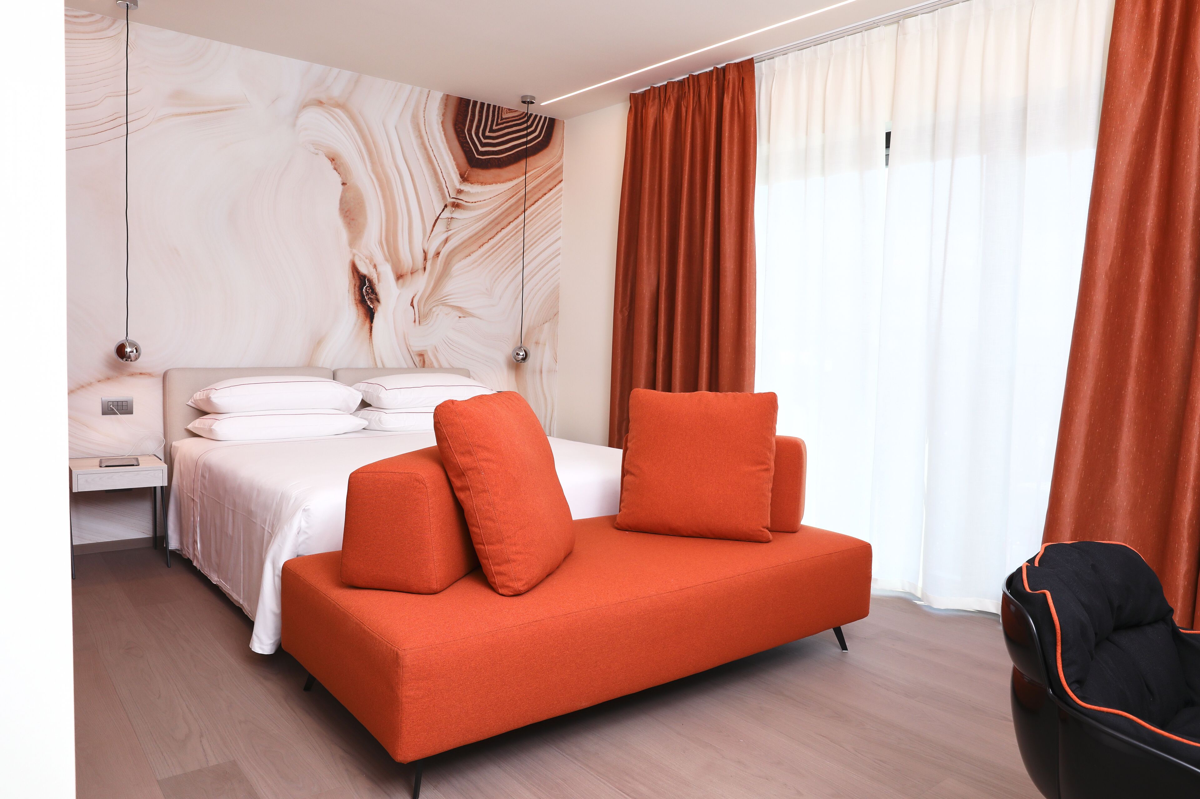 A modern hotel room with a bed, orange sofa, and a large abstract wall mural.
