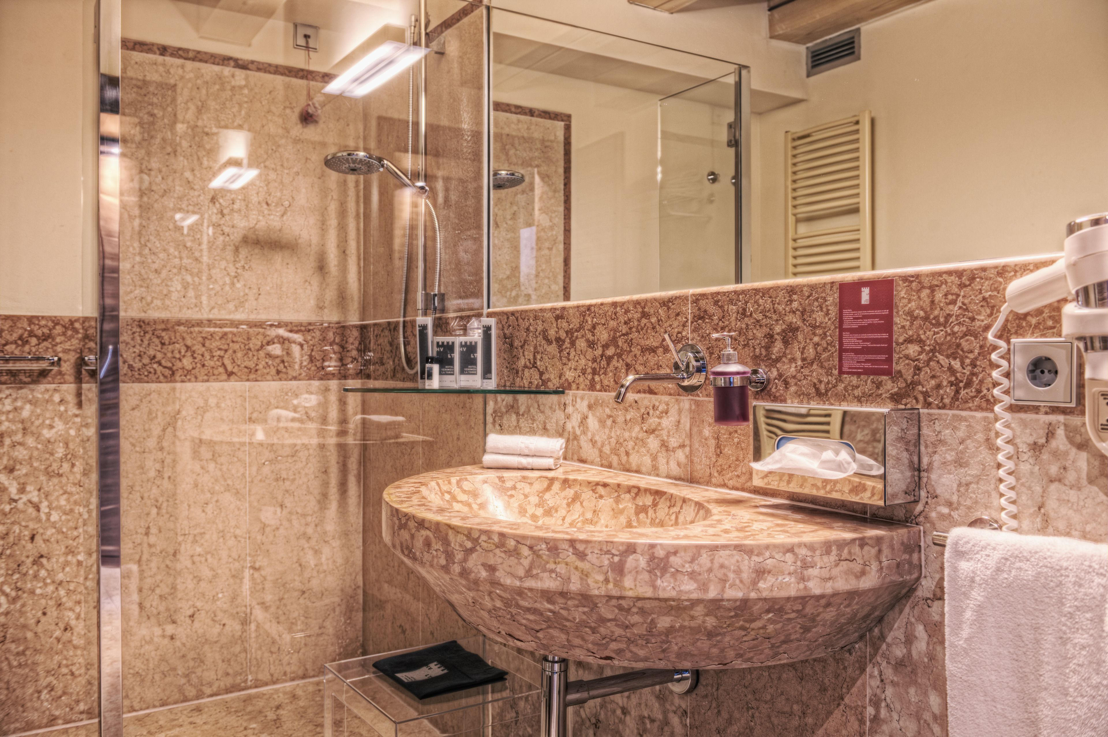 Un baño con lavamanos de mármol, cabina de ducha con vidrio y un espejo.