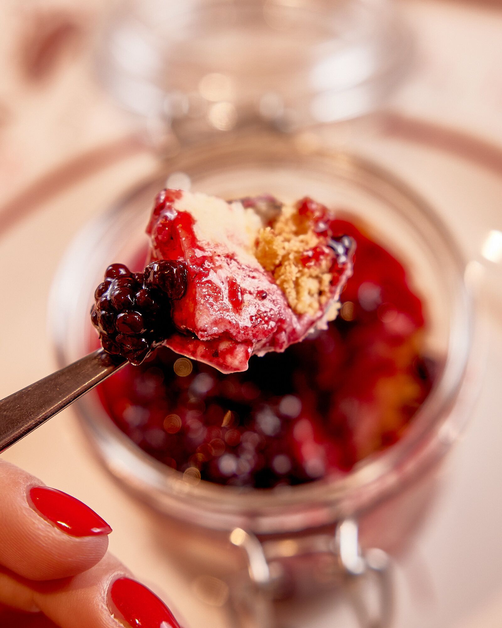 Une cuillerée de dessert aux fruits rouges, recouverte d’une pâte friable, présentée au-dessus d’un bocal rempli d’un dessert similaire.