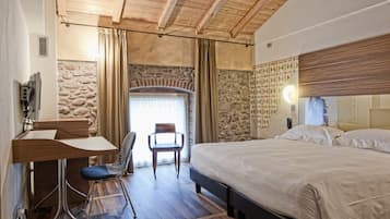 Une chambre avec un plafond en bois, un mur en pierre, un lit, un bureau avec une chaise et une fenêtre avec des rideaux.