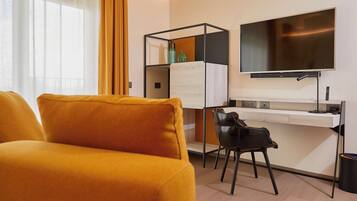 A hotel room with a sofa, a desk with a computer, a chair, and a TV mounted on the wall.
