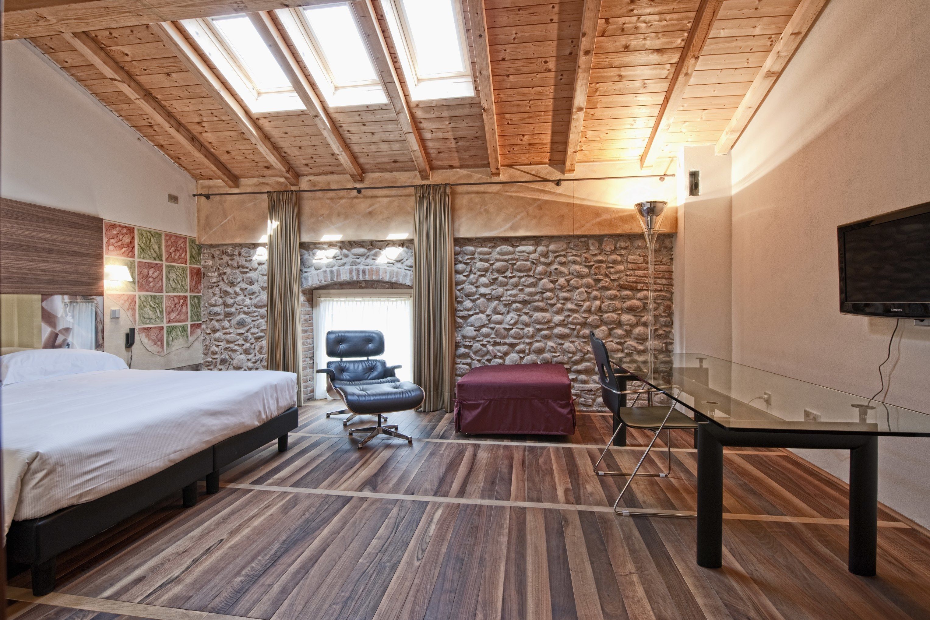 A bedroom with a bed, a chair, a table, and a stone wall.