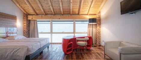 Een moderne slaapkamer met een houten plafond, een groot bed, een rode zithoek en een aan de muur bevestigde televisie.
