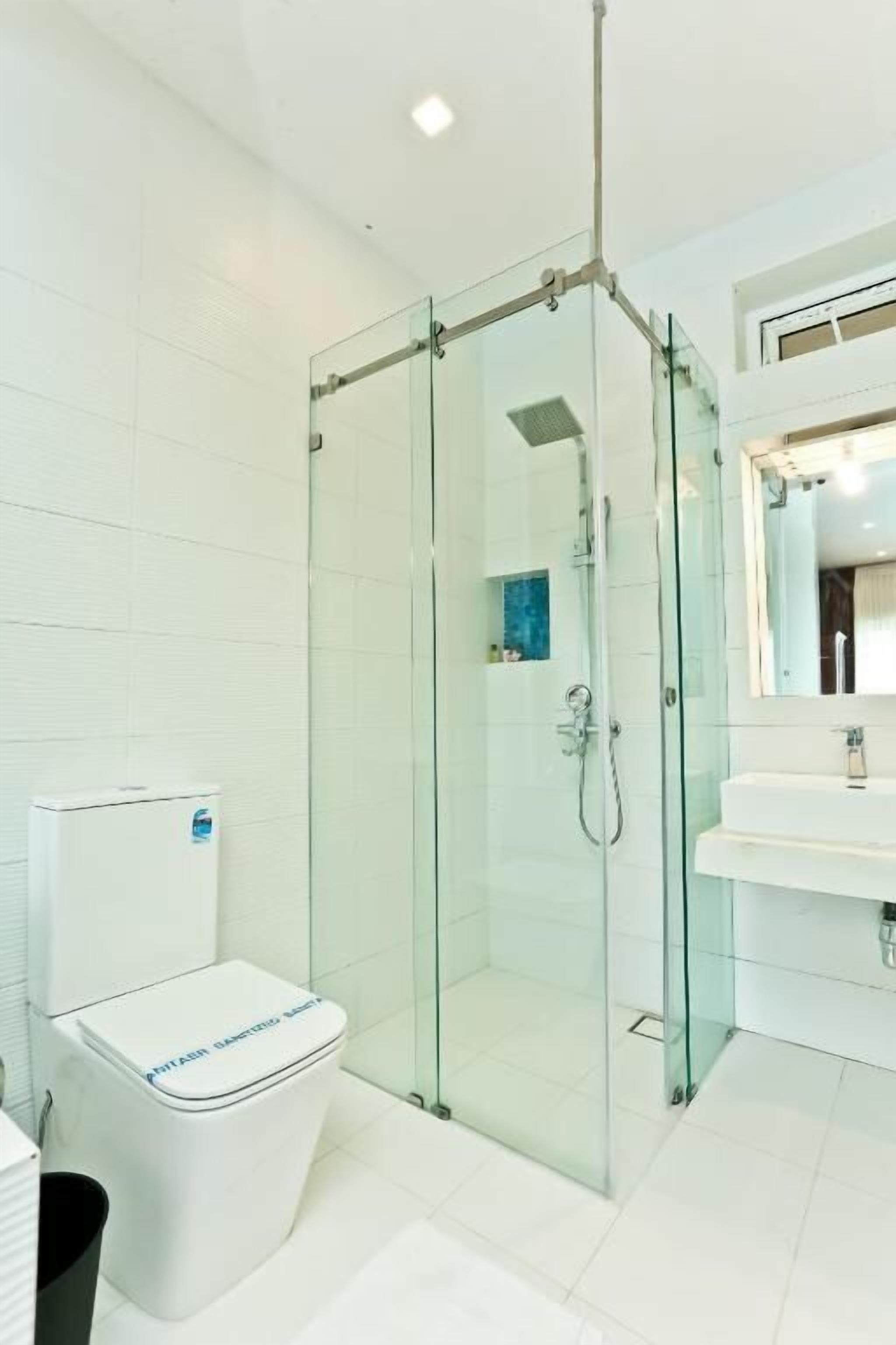 Un baño moderno con ducha de vidrio, inodoro blanco y lavamanos con espejo.