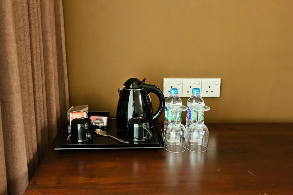 Un coin café comprenant une machine à café noire, un plateau, une boîte de capsules de café et trois verres sur une table en bois, le tout placé devant un mur de couleur beige.