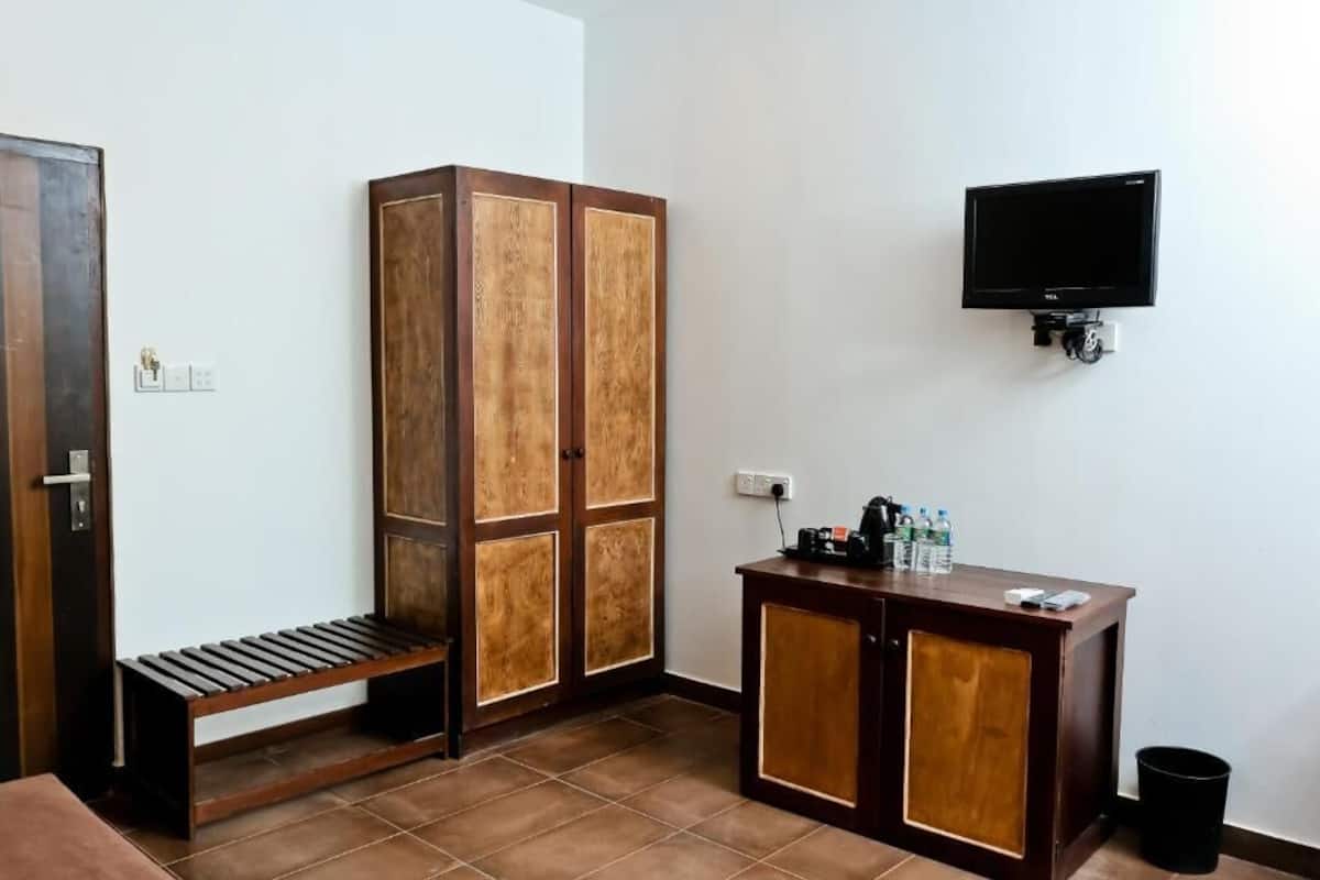 Ein Zimmer mit einem Holzschrank, einer Sitzbank, einem kleinen Holztisch mit Fernseher und einem Mülleimer.
