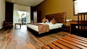 A modern hotel room with a large bed, wooden flooring, a desk, and a view of the outdoors.