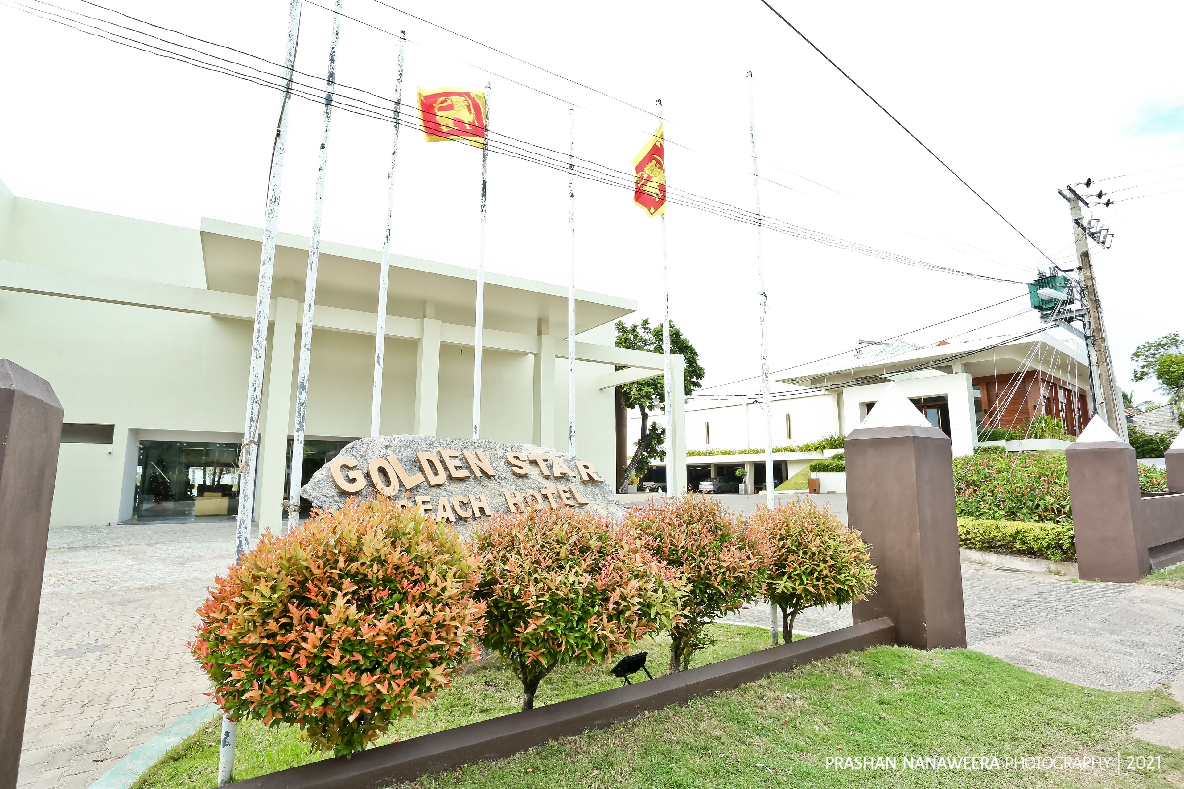 The entrance of Golden Star Beach Hotel with a sign, flag, and well-maintained landscaping.
