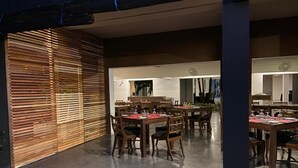 An indoor dining area with wooden slatted walls, multiple tables with chairs, and a tiled floor.