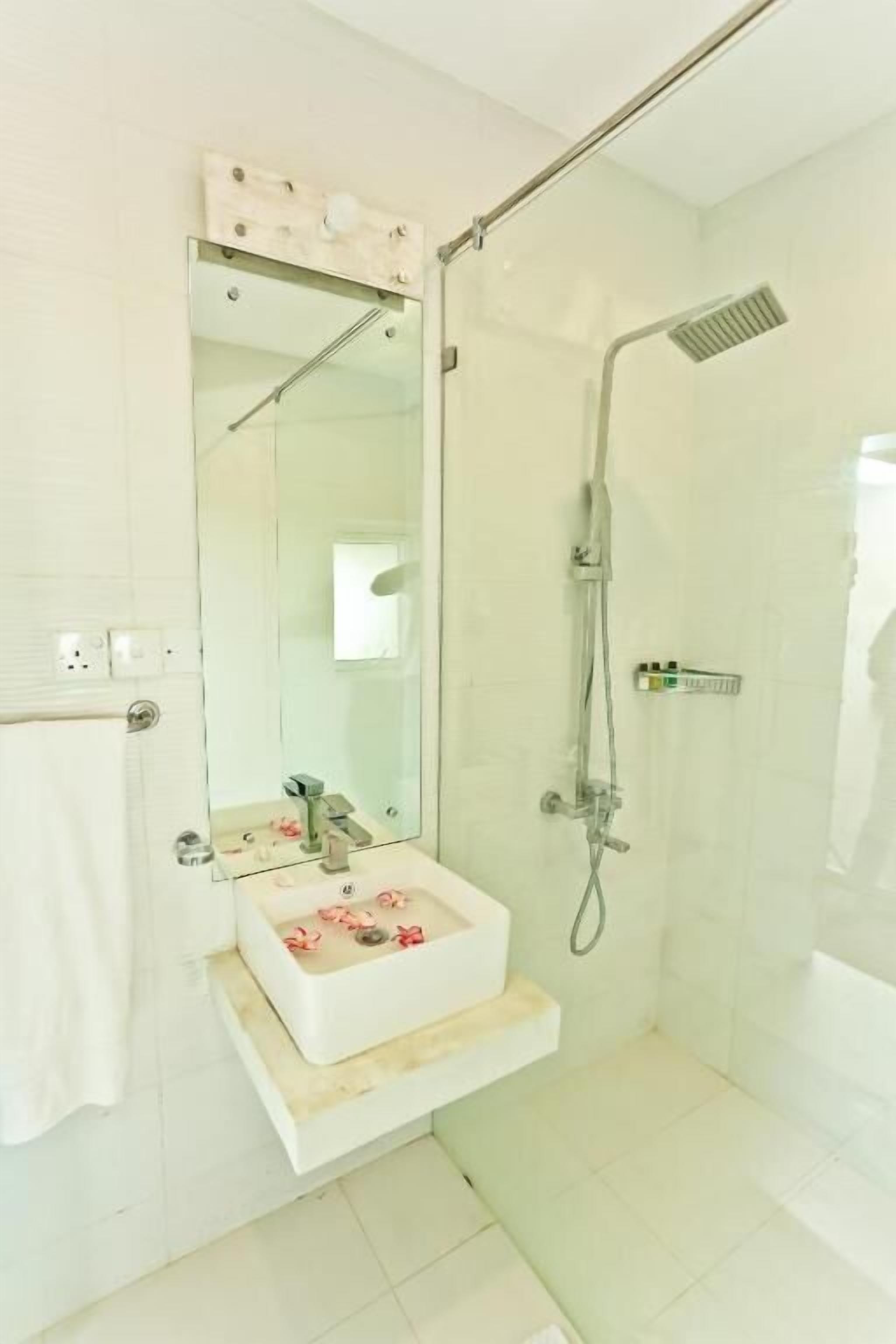 Un baño moderno con ducha envuelta en vidrio, un lavabo blanco con espejo y un perchero para toallas.
