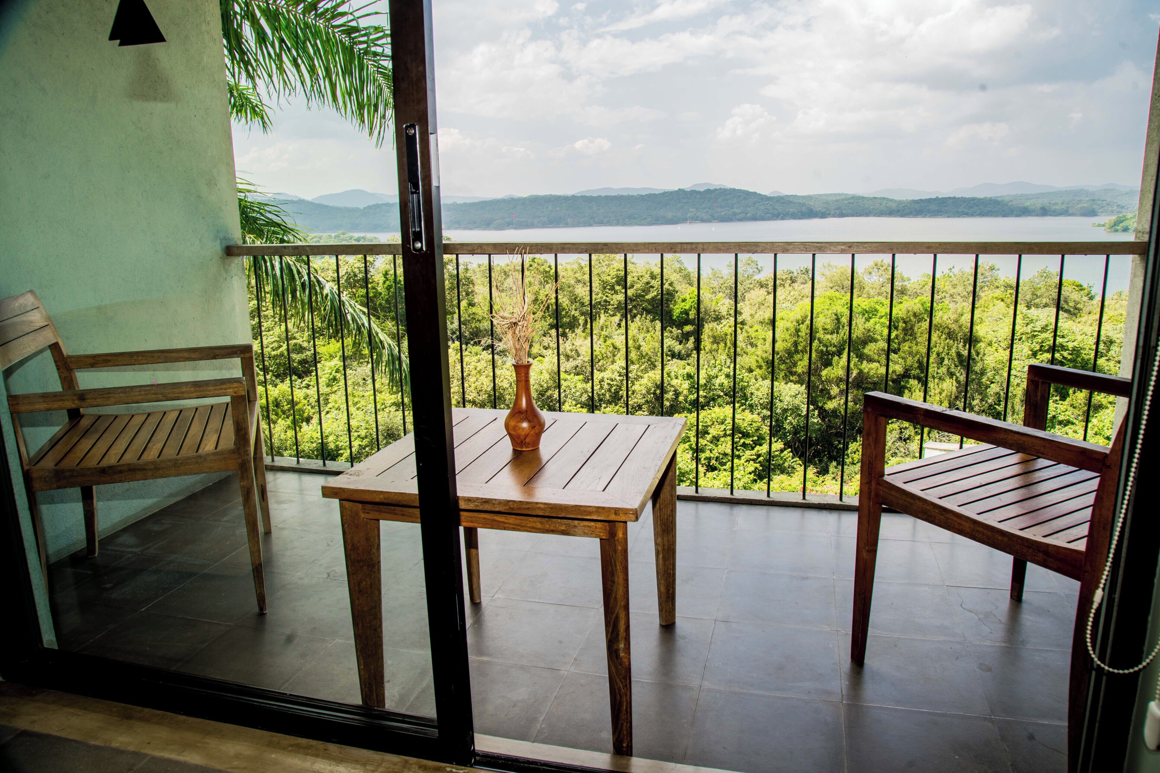 Un balcón con una mesa y sillas de madera, un jarrón y vistas a un lago y montañas.